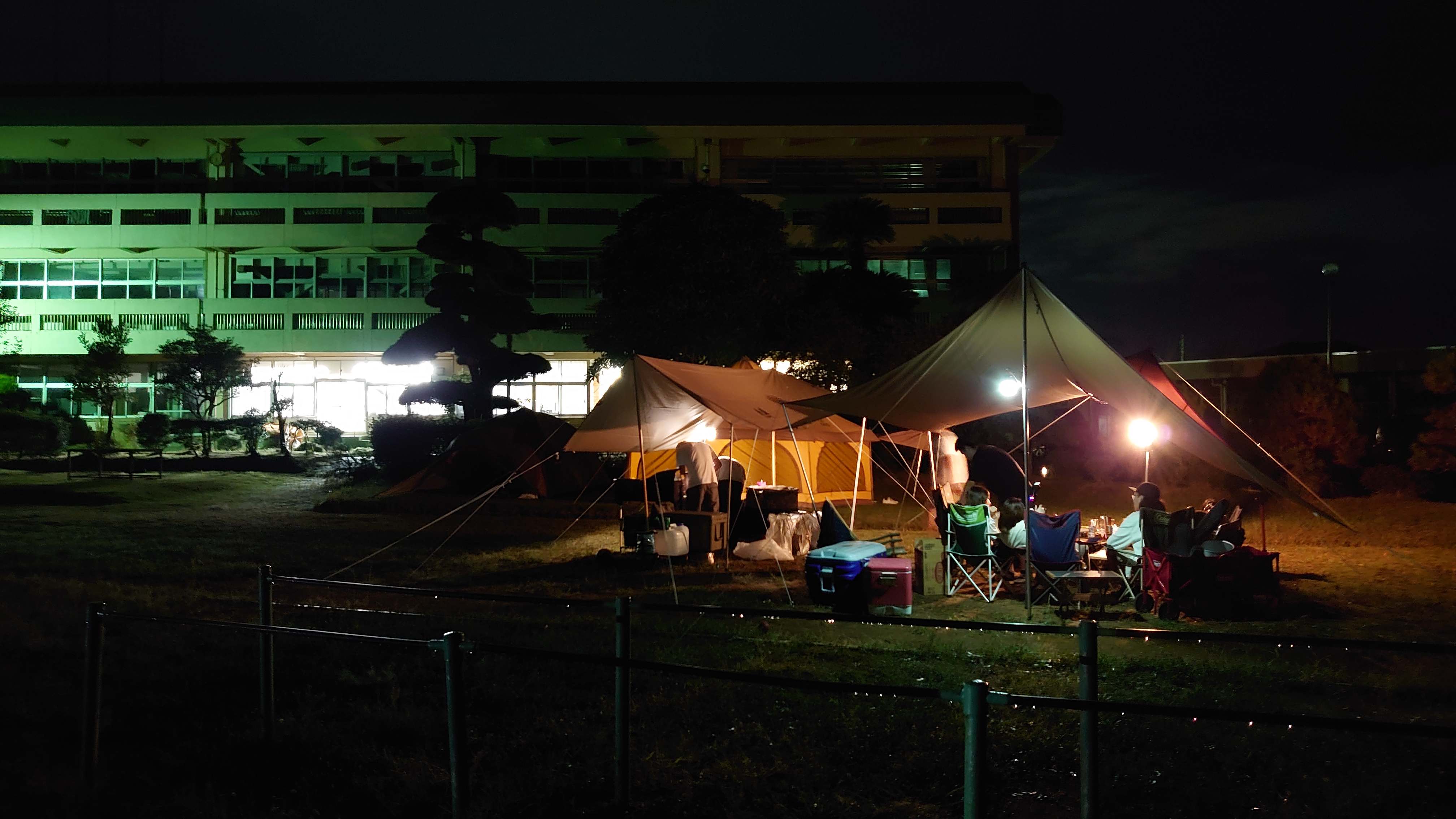 夜のキャンプ風景 - ライトアップされた校舎を背景にした幻想的な夜キャンプ